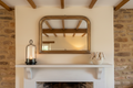 Tall lantern and bird bowl on a cottage mantelpiece with exposed stone wall and vintage mirror